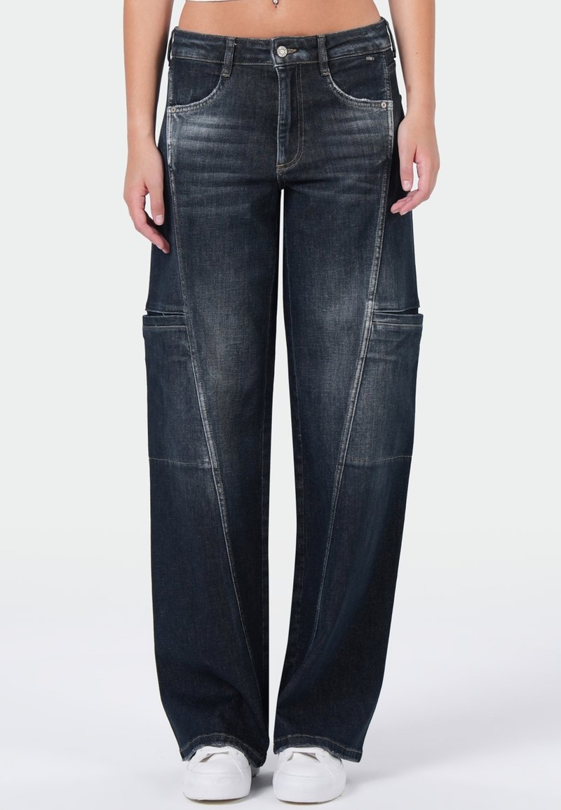 Donkerblauwe wijdetopje jeans met een vervaagde textuur, voorzakken en contrasterende stiksels. Draag ze met witte sneakers, wat de casual uitstraling benadrukt.