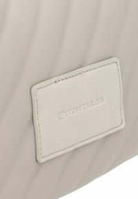 Borsa bianca testurizzata con un design ondulato. Presenta un'etichetta rettangolare in rilievo con la scritta "TOM TAILOR" e un bordo cucito.