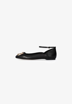 Scarpa piatta in pelle nera con punta affusolata, cinturino alla caviglia con fibbia e decorazione ornamentale dorata sulla punta.