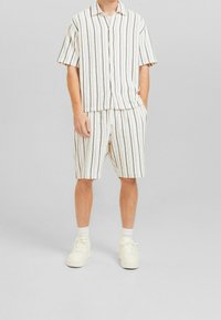 Lyhythihainen kauluksellinen paita ja siihen sopivat shortsit, joissa on pystysuuntaiset tummat raidat kermaisessa värissä. Valmistettu kevyestä kankaasta; rento istuvuus.