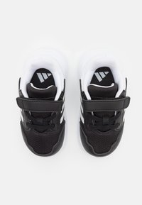 Chaussures de sport noires et blanches avec un dessus en mesh et synthétique, présentant une sangle à crochets et boucles, des lacets et un logo sur la semelle intérieure.