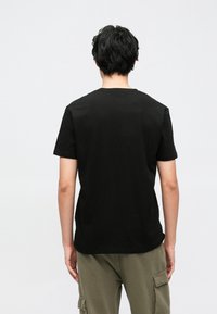 T-shirt preta de manga curta feita de algodão, com gola redonda clássica e textura suave. Usada com calças cargo verde-oliva.