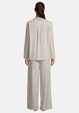 Donna con coda di cavallo scura vista di spalle, indossa una camicia a maniche lunghe grigio chiaro e pantaloni a gamba larga abbinati, su sfondo semplice.