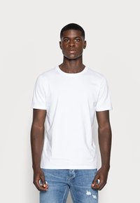 Weißes Baumwoll-T-Shirt mit Rundhalsausschnitt und kurzen Ärmeln, kombiniert mit hellblauen, verwaschenen Jeans. Glatte Textur, lässige Passform.