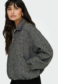 Veste grise à motif chevrons avec une fermeture éclair, des manches longues, des poignets côtelés et des poches latérales, dotée d'un col avec revers.