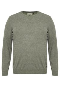 Crewneck genser i olivengrønn, laget av myk, teksturert stoff. Har lange ermer og ribbestrikkede mansjetter og hem med et merke nederst til venstre.