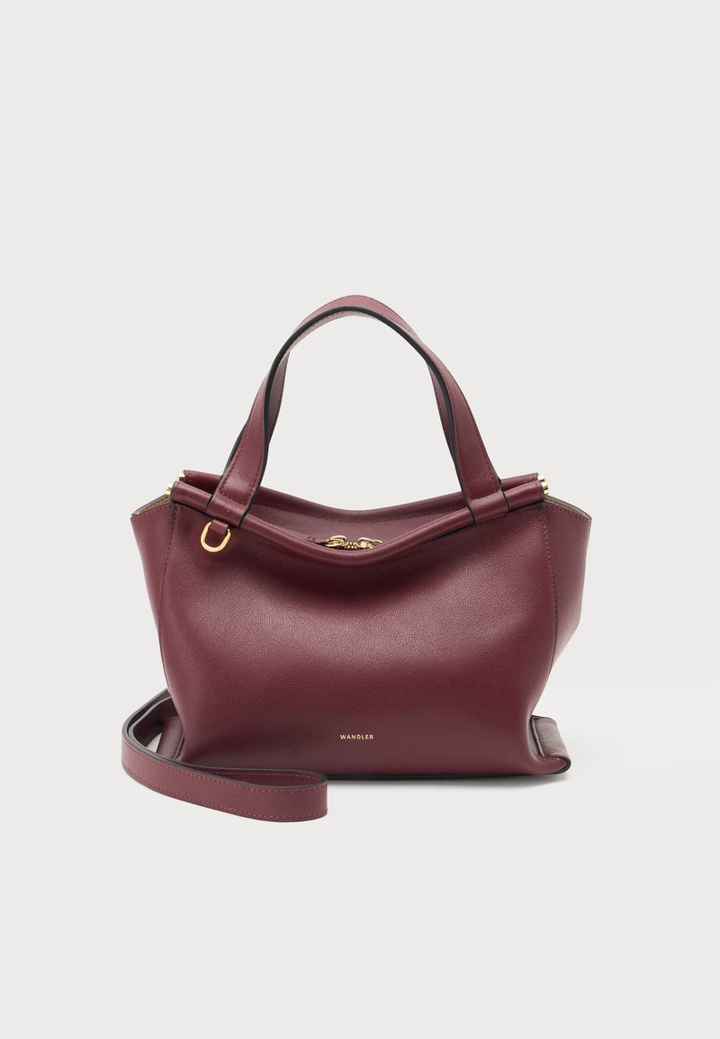 Sac à main en cuir rouge foncé avec deux poignées, une bandoulière détachable, ainsi que des détails zippés et un logo dorés sur fond blanc.