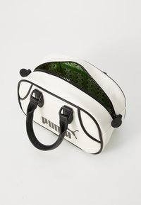 White PU handbag with black accents, rounded shape, dual handles, and a green patterned interior. Features a top zipper closure.
