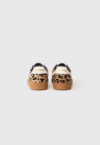 Tenisice s uzorkom leoparda, od nubuk kože, crnim detaljima i smešim gumiranim đonom. Imaju beli tab na peti s "Reebok" oznakom.