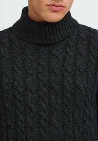 Pullover grigio scuro a maglia rasata con colletto alto a coste; presenta motivi spessi e testurizzati e un aspetto morbido e tessuto.