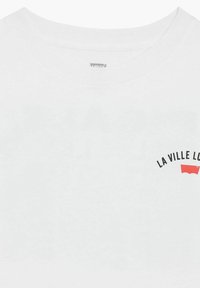 Vit bomull t-shirt med rund hals, med svart text och en röd grafisk logotyp. Slät textur, enkel design för avslappnad användning.