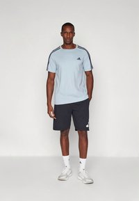 Ανοιχτό γαλάζιο αθλητικό μπλουζάκι με μαύρες ρίγες στα μανίκια, σε συνδυασμό με σκούρο σορτς που έχει λευκές λεπτομέρειες. Το υλικό φαίνεται λείο και διαπνέον.