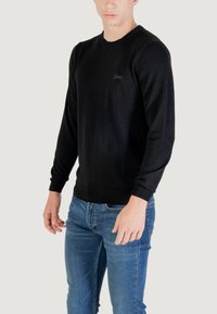 Maglione nero a maglia con scollatura rotonda e maniche lunghe. Leggeri dettagli sul petto. Abbinato a jeans in denim blu.