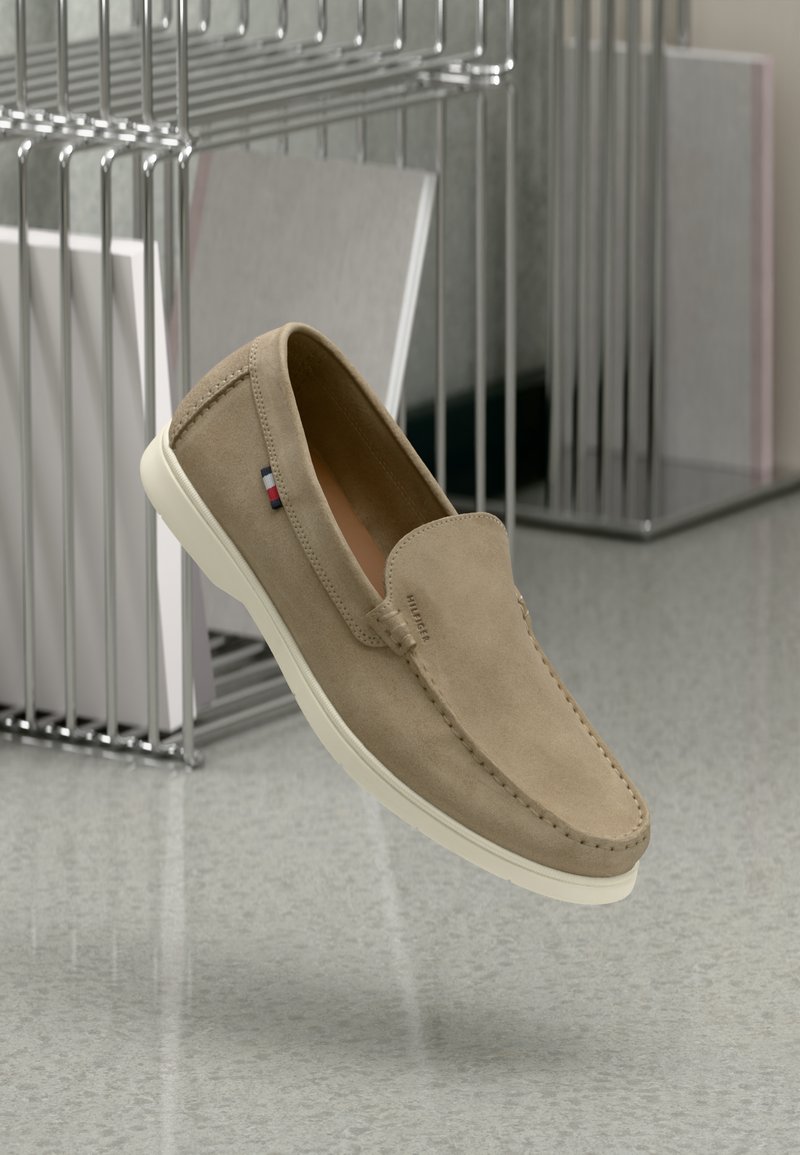 Tan suede slip-on shoes with white rubber sole, featuring subtle stitching and a branded accent on the side. Lightweight and contemporary design.