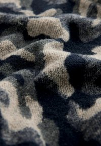 Close-up van zachte stof met een camouflagepatroon in tinten van zwart, grijs en beige, die de textuur en lichte plooien laat zien.