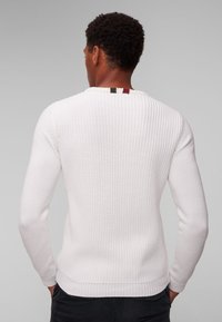 Maglione bianco a maglia con texture a coste, maniche lunghe e un accento a strisce in rosso, verde e nero sul colletto.