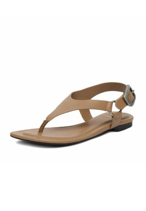 Beige flache Sandale mit T-Riemen, verstellbarer Metallschnalle und gepolsterter Sohle auf weißem Hintergrund.