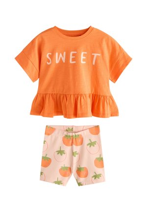 Haut orange à manches courtes avec texte "SWEET" et ourlet à volants, associé à un short rose clair imprimé de fruits orange avec des feuilles vertes.