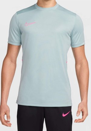Homme portant un t-shirt de sport gris clair à manches courtes avec un logo Nike rose et un short noir avec un logo Nike rose, debout les bras détendus.