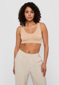 Seno beige senza fili con scollatura rotonda, tessuto morbido e elasticizzato, e spalline larghe. Abbinato a pantaloni beige chiaro a righe sottili.