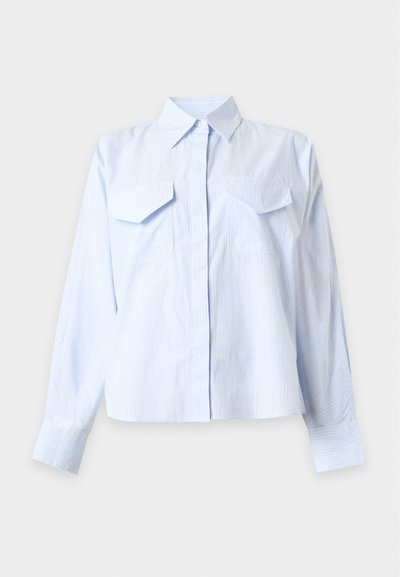 Chemise bleu clair à manches longues avec boutons, fines rayures verticales et deux poches poitrine à rabat sur fond blanc.