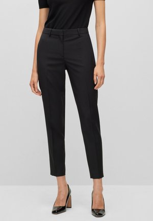 Pantalon noir ajusté avec une coupe slim, devant plat, passants de ceinture et poches latérales. Tissu lisse avec un éclat subtil, à associer avec des talons noirs.