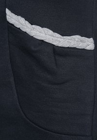 Marinfärgad tyg med en texturdetalj som har en grå flätad accent på fickan. Fickan är sydd i plagget.