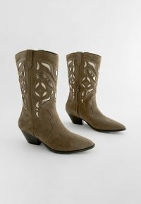 Bruna mockaskinnsboots i westernstil med spetsiga tår, utskurna mönster och en blockklack i medelhöjd. Siddragkedja för enkel av- och påtagning.