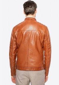 Giacca in pelle marrone con finitura testurizzata, polsini con zip e dettagli sulla cucitura. Design classico con una silhouette aderente.