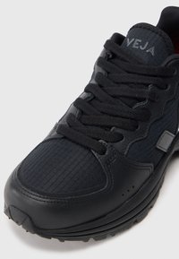 Κοντινό πλάνο μαύρου παπουτσιού VEJA με υφή ύφασμα, δερμάτινες λεπτομέρειες και μαύρα κορδόνια σε λευκό φόντο.