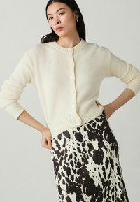 Ivory gebreide cardigan met geribbelde zoom en zes knopen, gecombineerd met een zwart-wit gestippelde rok, met een soepele stofstructuur.