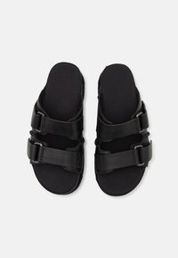 Sandales noires avec deux larges brides et boucles ajustables. Doublure en tissu doux, semelle plate et design minimaliste. Idéales pour un usage décontracté.