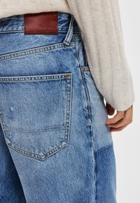 Hellblaue Jeans aus Denim mit einem Lederlogo-Patch auf der Rückseite, ausgestattet mit einem Standard-Taschendesign und leichter Verblassung entlang der Nähte.