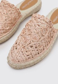 Mules de esparto tejidos en rosa claro, con intrincados patrones florales, material de fibra natural y una suela de yute texturizada.