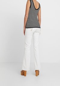 Gestreifes schwarz-weißes Tanktop mit tiefem V-Ausschnitt auf der Rückseite, kombiniert mit weißen, ausgestellten Jeans und beigen Plateausandalen.
