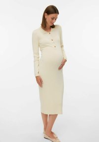 Ribbad, krämfärgad mammaklänning med krage, knäppning framtill, långa ärmar och en figursydd silhuett för att rymma en gravidmage.