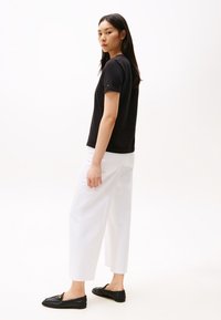Fekete pamut rövid ujjú póló, fehér, bőszárú nadrággal és fekete bebújós cipővel párosítva, egyszerű dizájnnal és minimális díszítéssel.