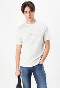 Ανοιχτό γκρι βαμβακερό t-shirt με κρουά ντεκολτέ, που διαθέτει ένα μικρό λογότυπο "LES DEUX" στο στήθος, συνδυασμένο με σκούρα μπλε τζιν.