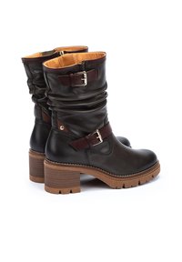Botas de cuero marrón hasta el tobillo con un diseño relajado, que cuentan con una correa de hebilla y un tacón grueso, con una suela texturizada y un forro interior en tono marrón claro.