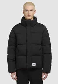 Schwarze Steppjacke mit hohem Kragen, gestepptem Design und Seitentaschen. Verfügt über ein Logo-Patch am Saum und einen Reißverschluss vorne.