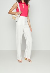 Top fucsia senza maniche con dettaglio a chiave, abbinato a pantaloni bianchi a vita alta. Gli accessori includono una borsa intrecciata e sandali con cinturini.