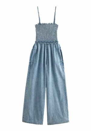 Combinaison en denim avec corsage smocké, fines bretelles réglables, coupe à jambes larges, couleur bleu clair, et deux poches latérales.
