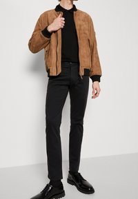 Brown suede bomber jacket with ribbed cuffs, paired with a black polo shirt, black slim-fit pants, and black lace-up shoes.