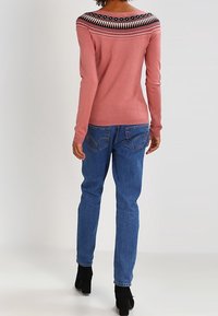 Pull rose à manches longues avec un empiècement noir à motifs, associé à un jean bleu et des bottines noires. Présente une silhouette ajustée et des poignets côtelés.