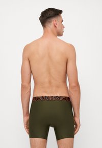 Olive green boxer shorts with a textured waistband featuring black and orange logo text. Smooth material, fitted design, short leg length.