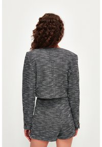 Chaqueta corta de tweed texturizado en blanco y negro con mangas largas, detalles de botones dorados, combinada con pantalones cortos a juego.