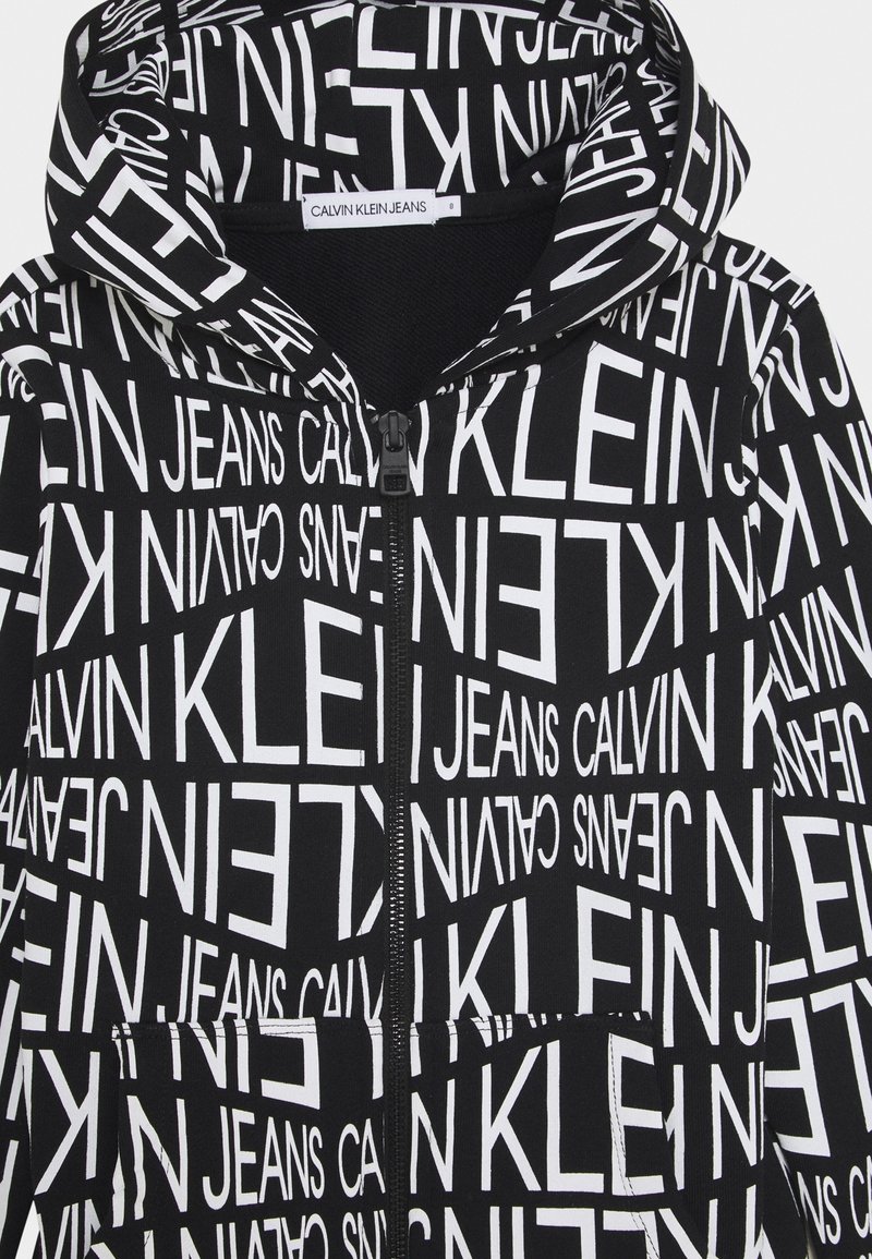 Felpa nera con zip caratterizzata da un audace testo bianco "CALVIN KLEIN JEANS" in varie oriеntazioni, con un tessuto testurizzato e tasche frontali.