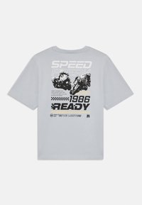 Šviesiai pilkas trumpomis rankovėmis marškinėliai, kuriuose pavaizduoti motociklų lenktynininkai ir tekstas "SPEED FREAK 1986 READY" juodais ir geltonais akcentais.