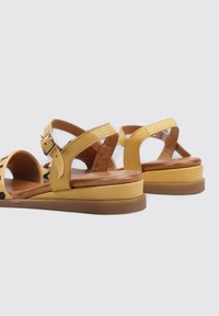 Sandales en cuir jaune avec des accents marron ; design ouvert, sangle avec détail de boucle, semelle rembourrée et semelle épaisse pour le soutien.