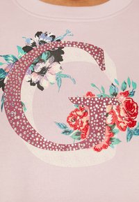 Sudadera de color rosa claro con una gran "G" adornada con flores en púrpura y acentos de strass. Fabricada en un tejido suave con diseños florales.